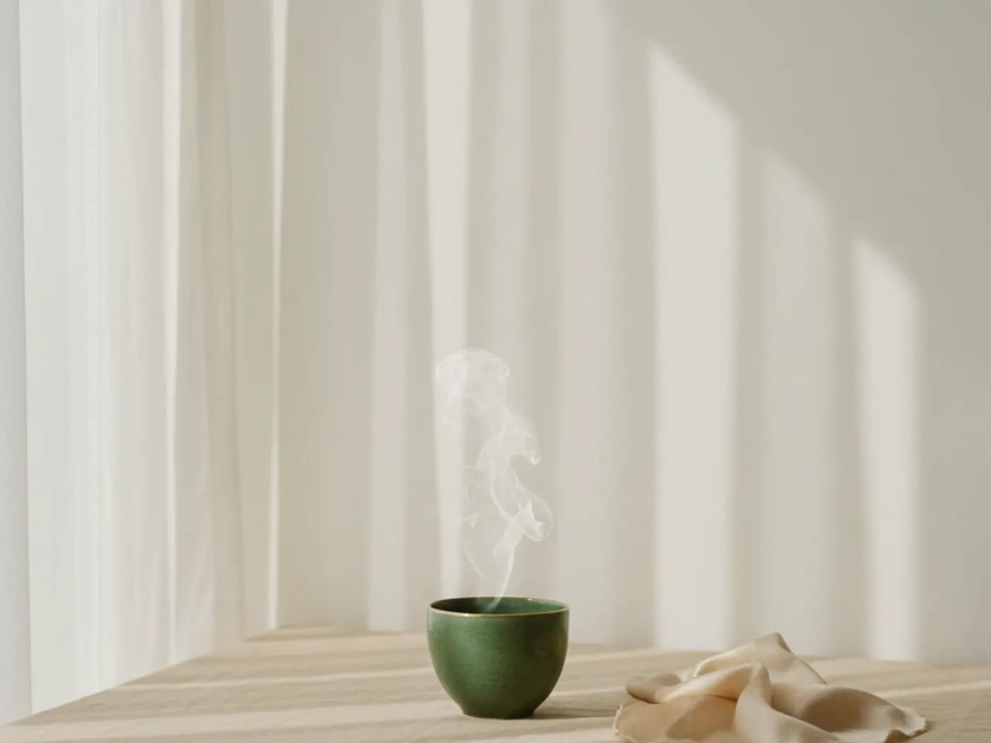 Eine dampfende Tasse Tee vor einem hellen Vorhang im Morgenlicht